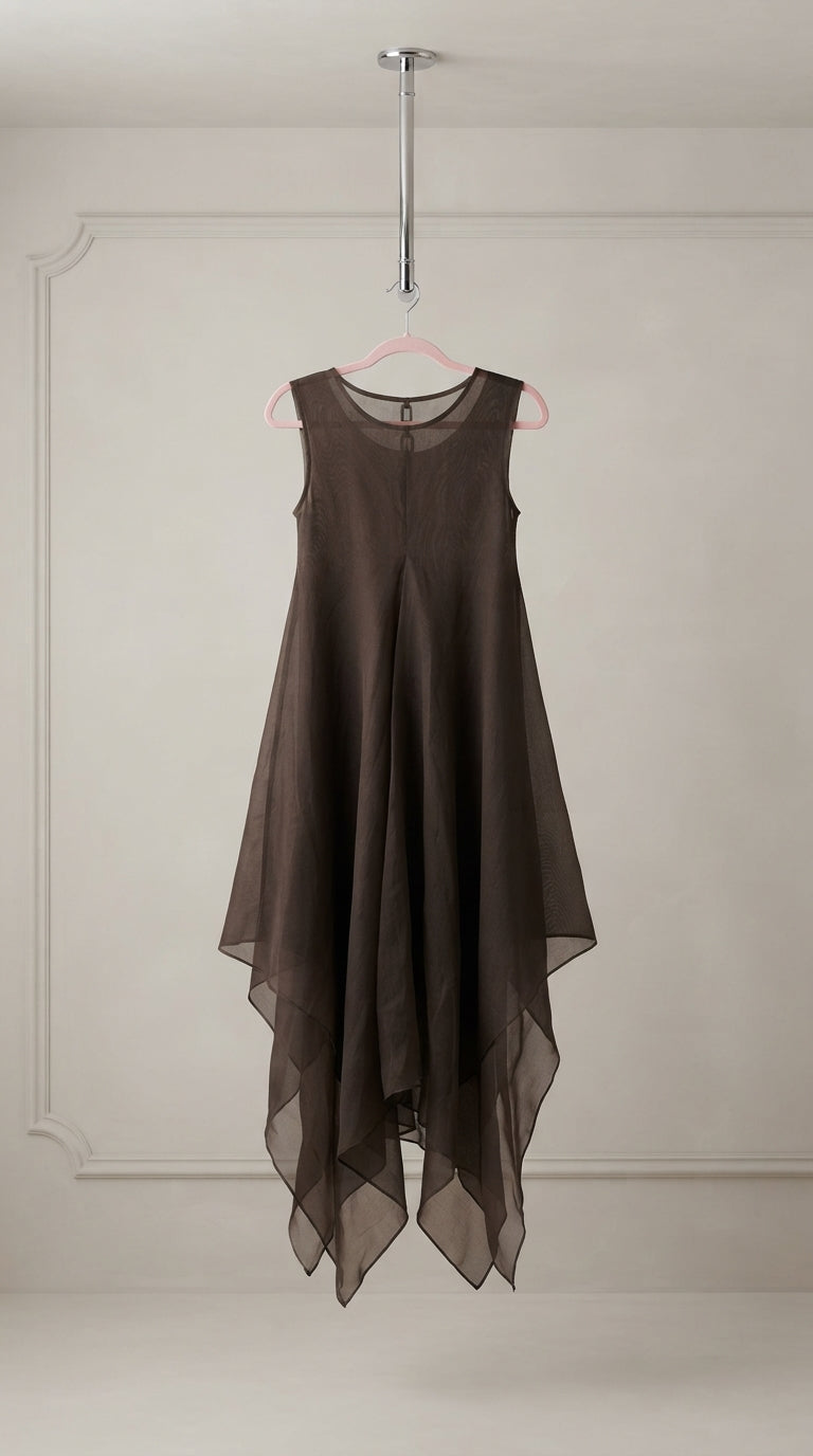 A sleeveless, high-low midi dress in a dark brown sheer mesh fabric, hanging on a pink hanger from a metal rod against a light beige wall with decorative molding.
