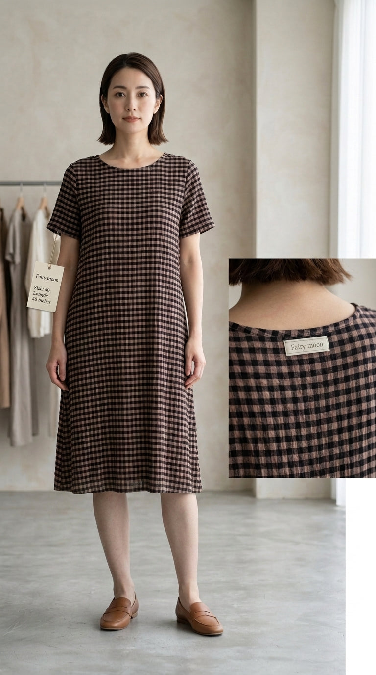 A woman stands indoors wearing a short-sleeve knee-length dress with a brown and black gingham check pattern. A small inset at right shows the back neckline and a brand label.