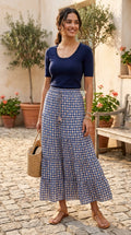 Woman wearing navy geometric print tiered maxi skirt with navy knit top and straw bag