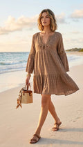Woman walking on beach in mocha plaid crochet lace tiered cotton mini dress with wicker bag and leather sandals — Luxmee Global Fashion