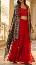 A woman models a traditional Indian outfit featuring a vibrant red crop top and wide-leg pleated pants, styled with a black and red patterned shawl draped over her shoulders.